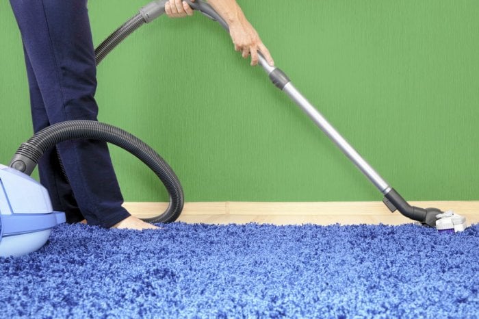 Someone running a vacuum cleaner on blue carpet
