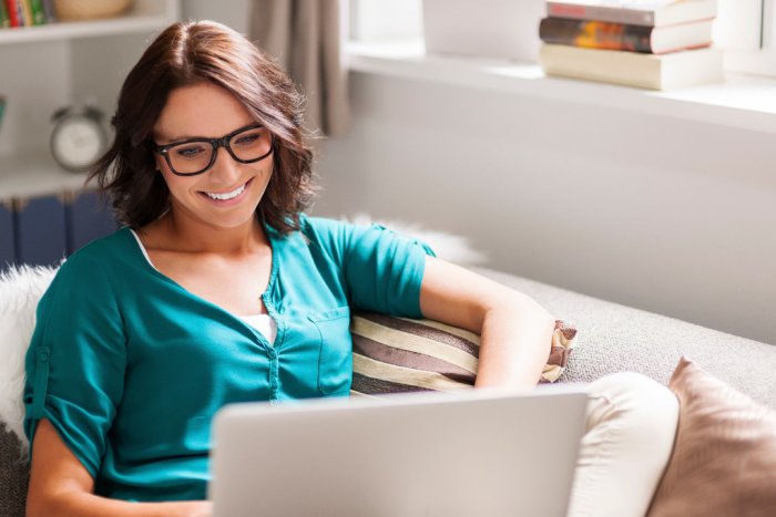 Woman in glasses sits on her sofa with laptop computer