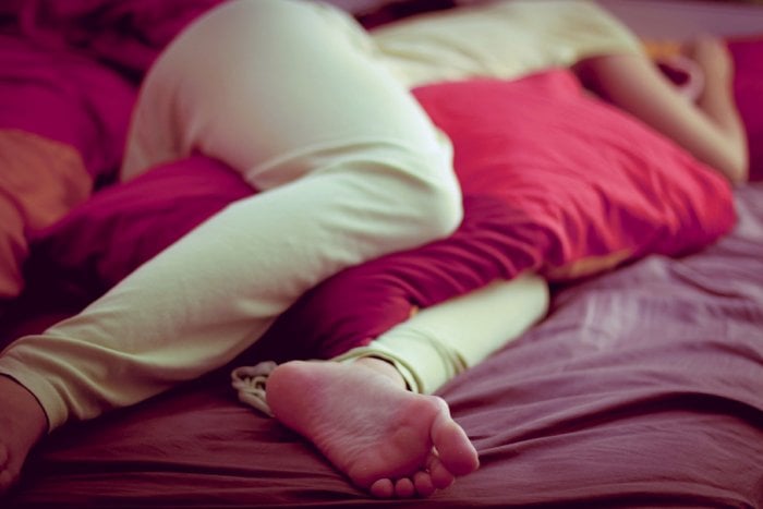 A woman sleeps with a pillow between her knees on a bed.