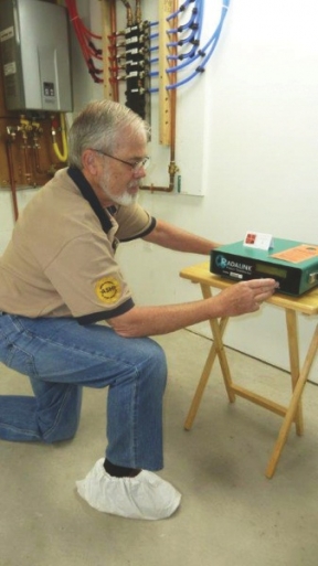 A man on bended knee sets up a radon detector that will monitor the amount of radon in a home