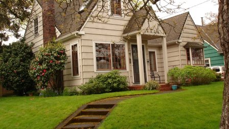 beige gable roof line house with portico porch with assending steps on a lawn.