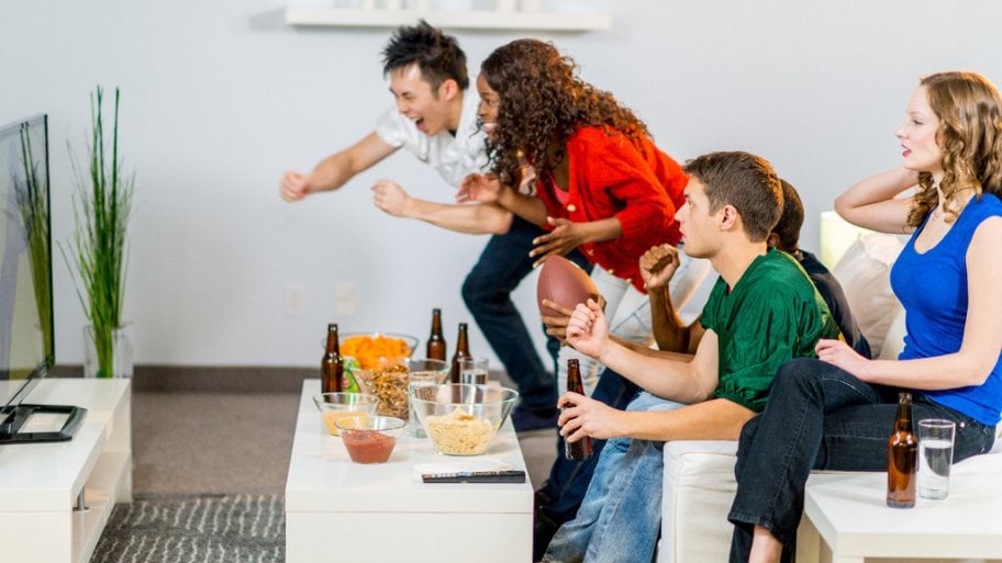 Friends on a couch drinking beer and watching a football game, two up and cheering