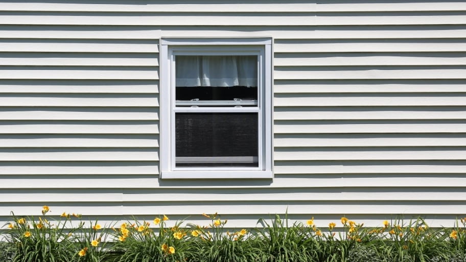a house with vinyl siding, a window and some yellow flowers