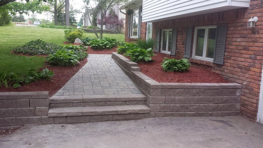 a rock wall and walkway to a brick house