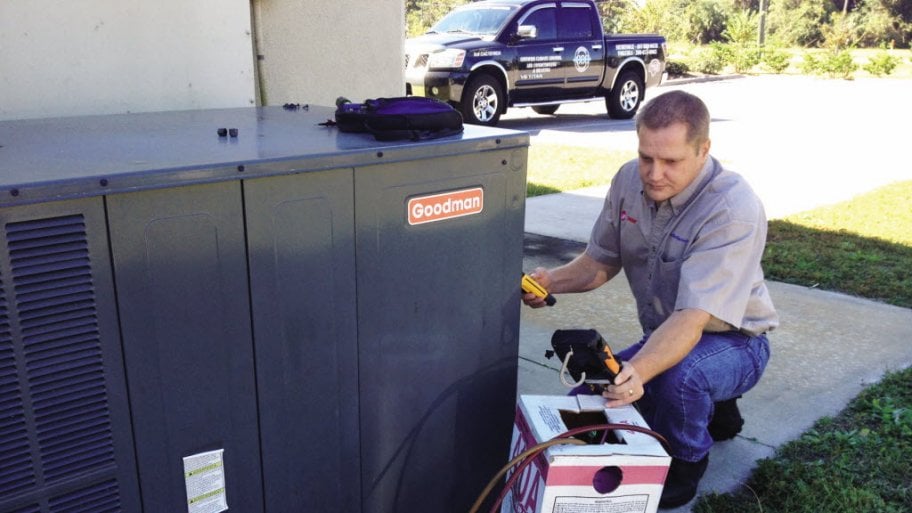 technician performs an outside service check on an air conditioning unit.