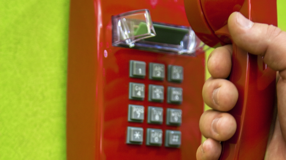 Red old landline telephone with hand grabbing phone on green wall