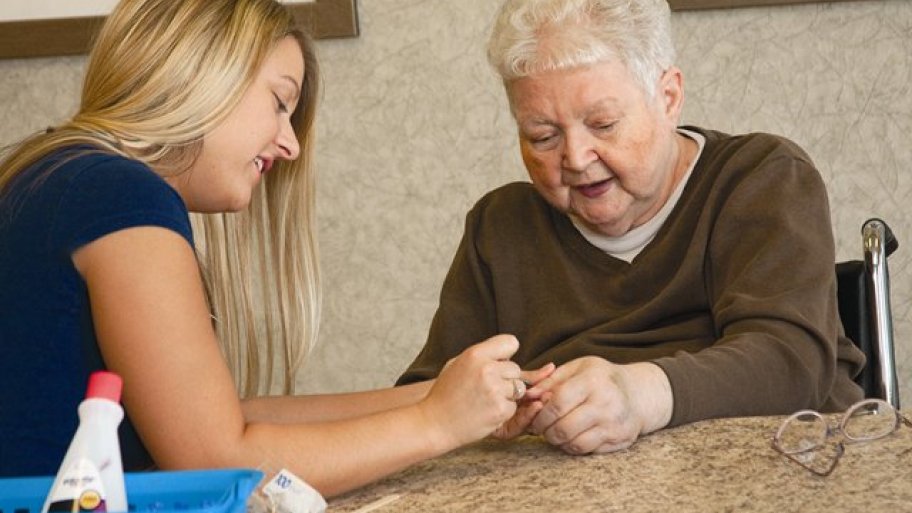 A young women gives a manicure to an elderly woman.