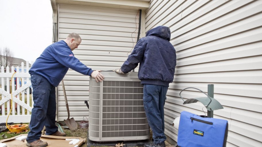 Two workers installing an a/c unit outside a home.