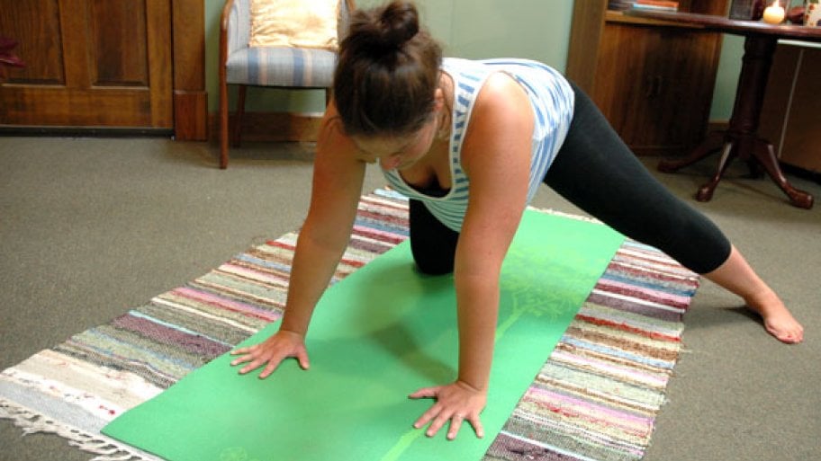A woman with one knee on a yoga mat and the other leg extended.