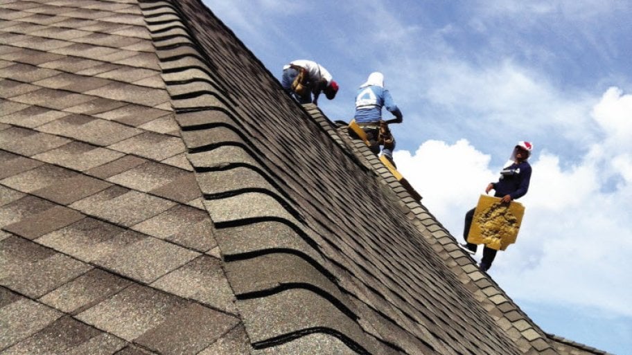 workers install asphalt shingles on roof